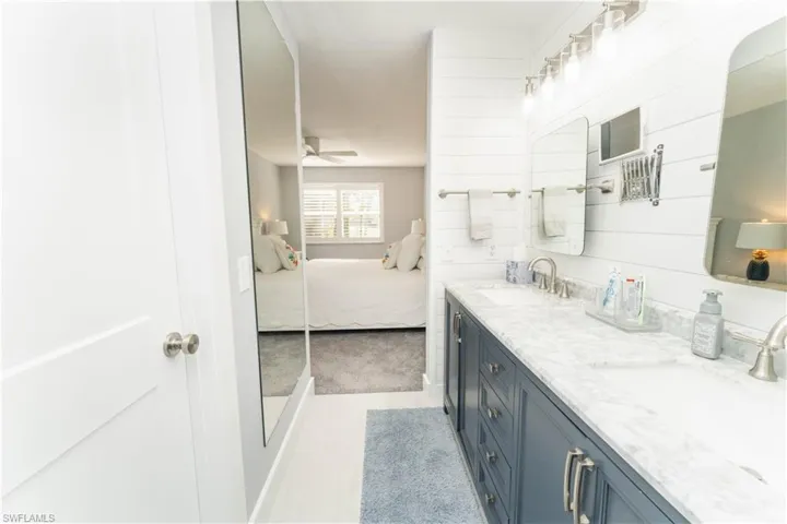 Ensuite bathroom with double vanity, light colored carpet, and ceiling fan
