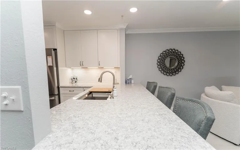 Kitchen with decorative backsplash, light stone countertops, white cabinetry, freestanding refrigerator, and a kitchen bar