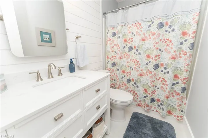 Full bath with vanity, a shower with curtain, wood walls, and light tile patterned flooring