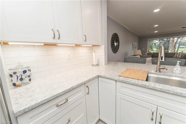 Kitchen with white cabinets, backsplash, light stone countertops, open floor plan, and crown molding