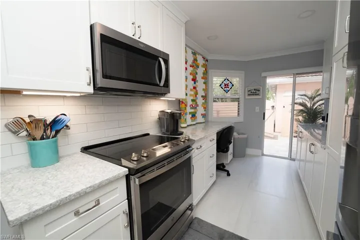 Kitchen featuring appliances with stainless steel finishes, white cabinets, tasteful backsplash, crown molding, and light stone countertops