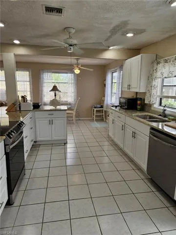 Kitchen with light tile patterned floors, visible vents, appliances with stainless steel finishes, white cabinetry, and a sink