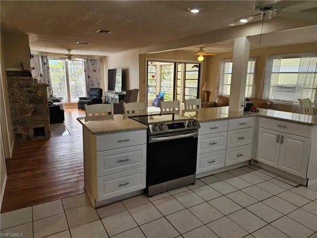 Kitchen featuring white cabinetry, open floor plan, stainless steel range with electric stovetop, light tile patterned floors, and a ceiling fan