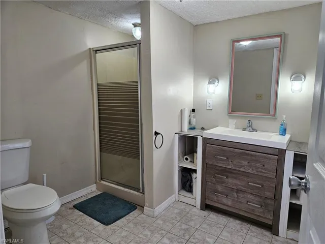Bathroom featuring tile patterned flooring, toilet, a textured ceiling, and a shower stall