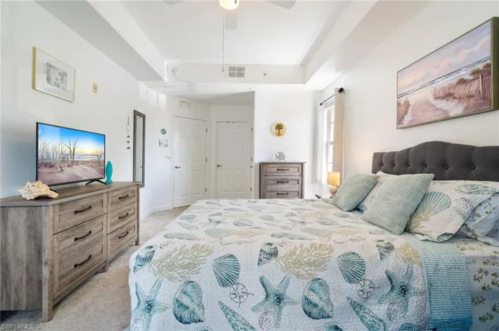 Bedroom featuring light carpet, a ceiling fan, and a tray ceiling