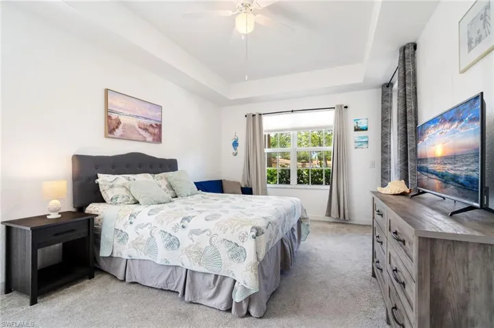 Bedroom featuring light colored carpet, a raised ceiling, and ceiling fan