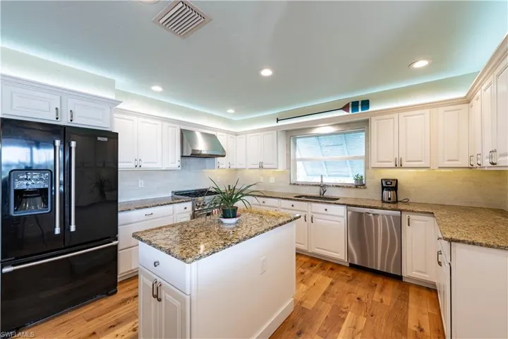 Kitchen featuring visible vents, wall chimney exhaust hood, a sink, white cabinetry, and stainless steel appliances