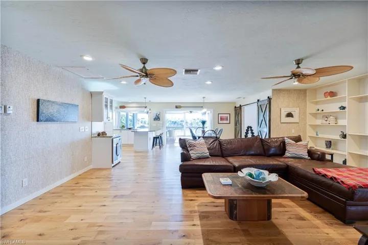 Living area featuring hardwood floors, wallpapered walls, ceiling fan, and a barn door