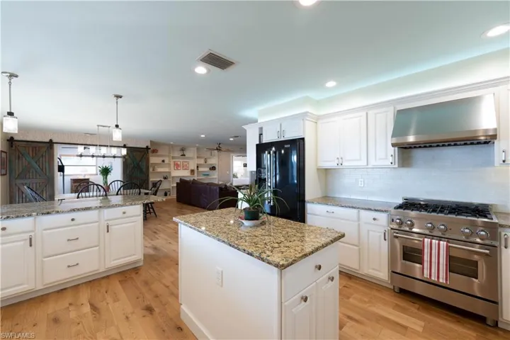 Kitchen featuring visible vents, black refrigerator with ice dispenser, a barn door, stainless steel range, and wall chimney range hood