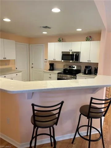 Kitchen with tile counters, white cabinets, a kitchen breakfast bar, and recessed lighting