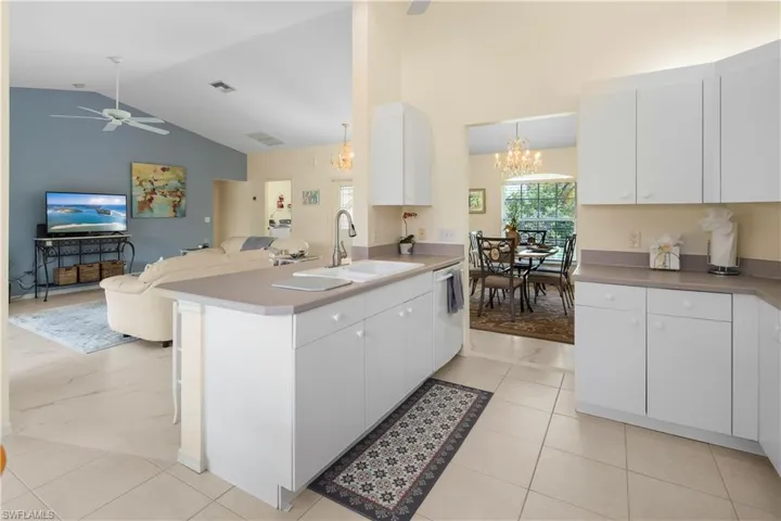 Kitchen featuring an island with double sink, white cabinetry, and light-toned countertops