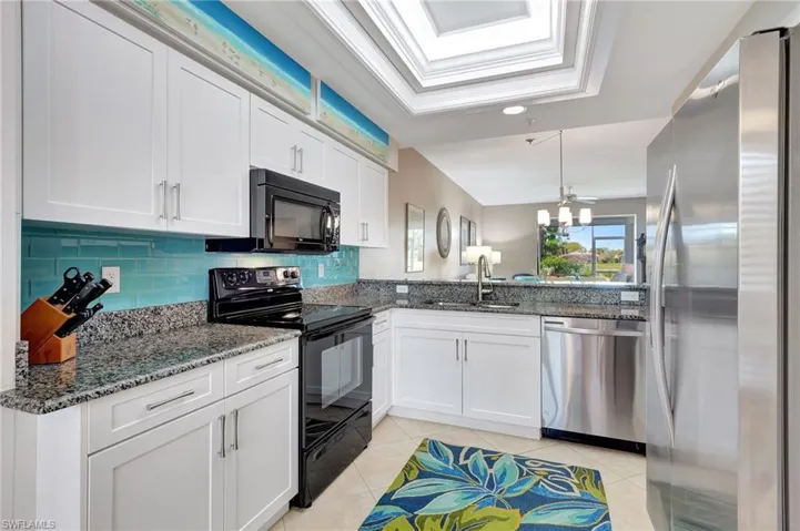 Kitchen with black appliances, dark stone counters, white cabinetry, hanging light fixtures, and ornamental molding