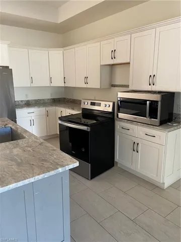 Kitchen with electric stove, white cabinetry, fridge, and light stone countertops