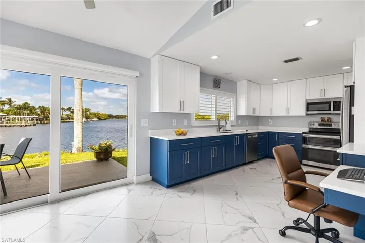 Kitchen with a river view, blue cabinetry, white cabinetry, quartz counter tops, stainless steel appliances, porcelain tile floors.  Built in desk on right side of photo.