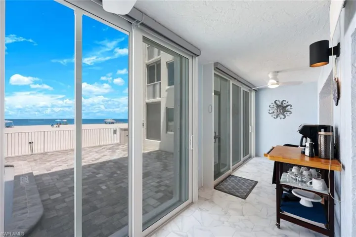 Sunroom with a water view, marble finish floors, a ceiling fan, and a textured ceiling
