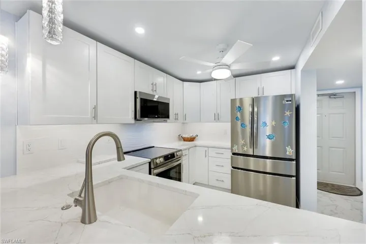 Kitchen with stainless steel appliances, light stone countertops, backsplash, recessed lighting, and marble finish flooring
