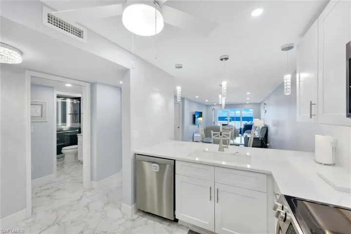 Kitchen featuring stainless steel appliances, white cabinets, light stone counters, light marble finish flooring, and a peninsula
