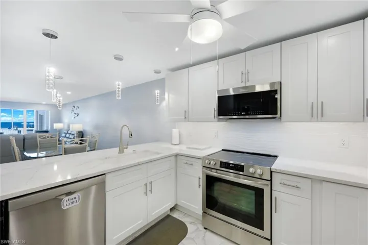 Kitchen featuring appliances with stainless steel finishes, light marble finish floors, tasteful backsplash, white cabinets, and light stone counters