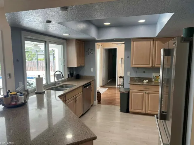 Kitchen featuring wood cabinetry, light-toned countertops, a stainless steel sink with a high-arc faucet, and a large sliding glass door overlooking a pool