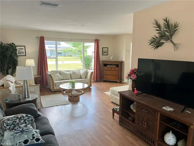 Wood-finish flooring throughout, featuring a large picture window with drapes, and an overhead light fixture