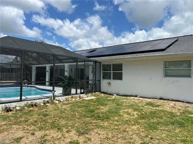 Screened swimming pool enclosure with a concrete deck, multiple windows, and solar panels on the roof
