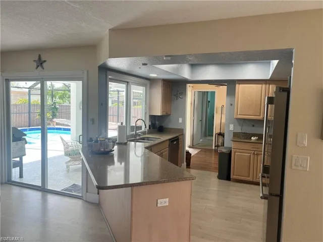 Spacious kitchen with wood-finish flooring, light wood cabinetry, and a curved peninsula with a stone-finish countertop