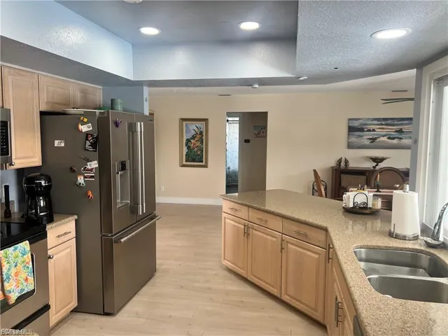 Kitchen featuring light wood-finish cabinetry, stainless steel appliances, and a curved island with an undermount sink and stone-finish countertop