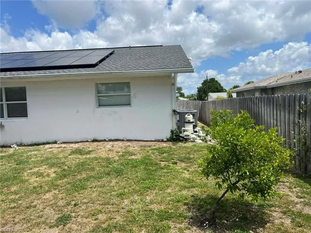 Rear exterior with solar panels, shingle roofing, and a privacy fence