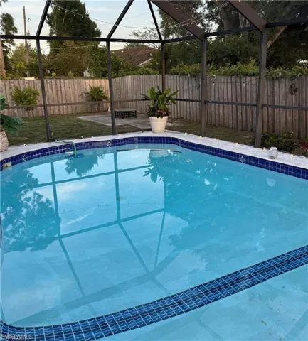 Screened enclosure featuring a swimming pool with blue tile accents and a privacy fence