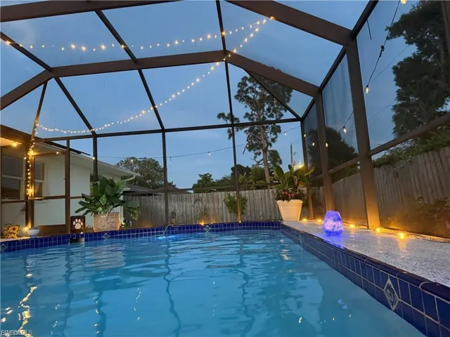 Screened pool enclosure with a blue tiled waterline, surrounding paved deck, and adjacent fencing