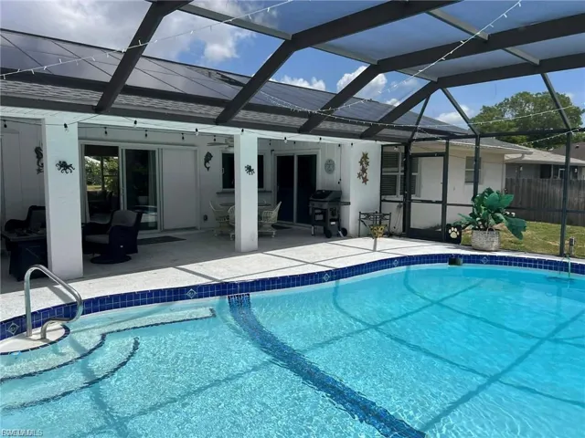 Screened outdoor pool area featuring a curved pool with integrated steps, a tiled pool deck, and sliding glass doors