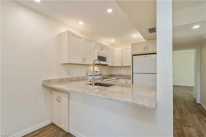 Kitchen featuring white cabinetry, white appliances, light stone countertops, and dark hardwood / wood-style floors