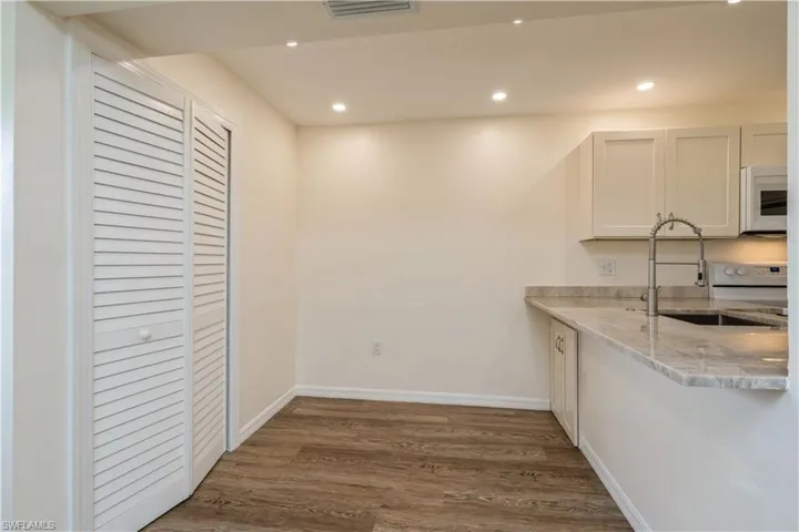 Kitchen featuring white appliances, light stone counters, white cabinetry, sink, and dark wood-type flooring