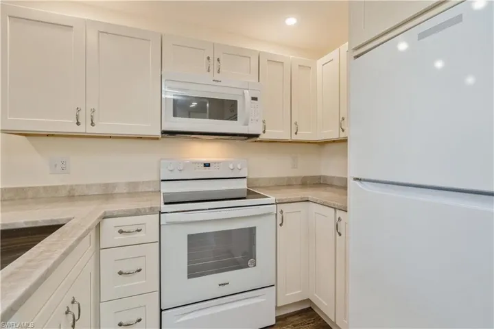Kitchen with light stone countertops, white appliances, and white cabinets