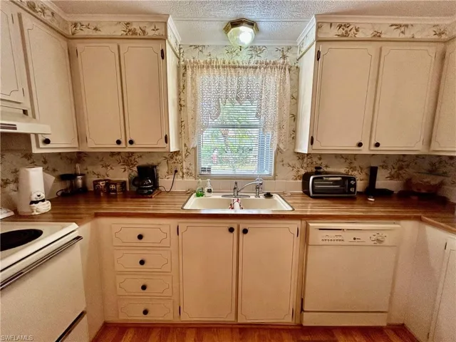 Kitchen with sink, extractor fan, a textured ceiling, light hardwood / wood-style floors, and white appliances
