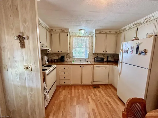 Kitchen with sink, light hardwood / wood-style floors, white appliances, and cream cabinetry