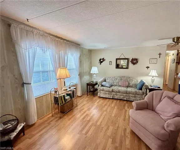 Living room with wood walls, light hardwood / wood-style flooring, ceiling fan, and a textured ceiling