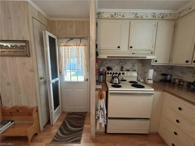 Kitchen with electric stove, light hardwood / wood-style floors, cream cabinetry, and ornamental molding