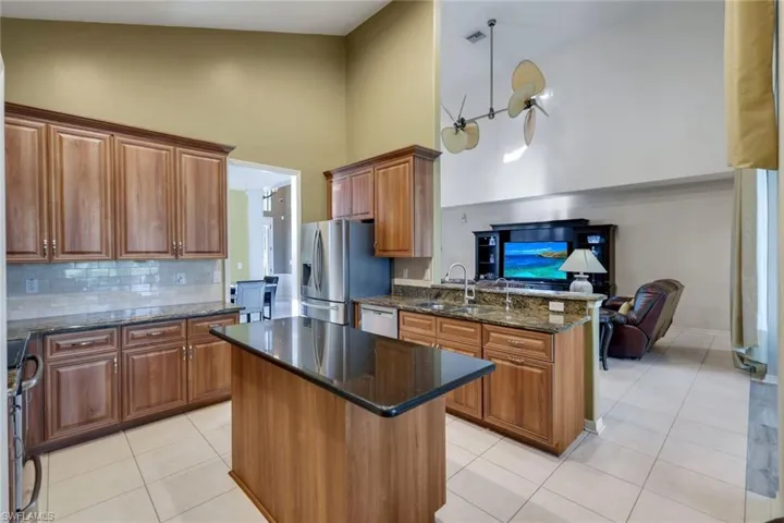 Eat in Kitchen featuring appliances with stainless steel finishes, a center island, high vaulted ceiling, and dark stone counters overlooking grand room.