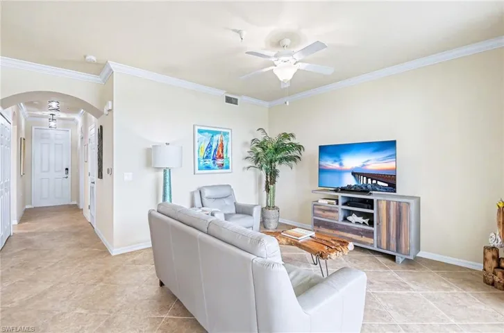 Open concept living area featuring tile flooring, crown molding, a ceiling fan, and an arched hallway entry