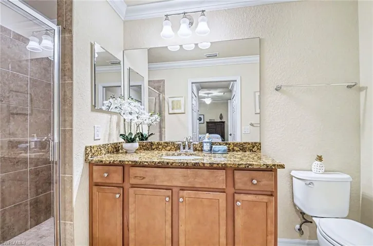 Bathroom featuring a wood-finish vanity with a stone countertop, an undermount sink, and a large mirror