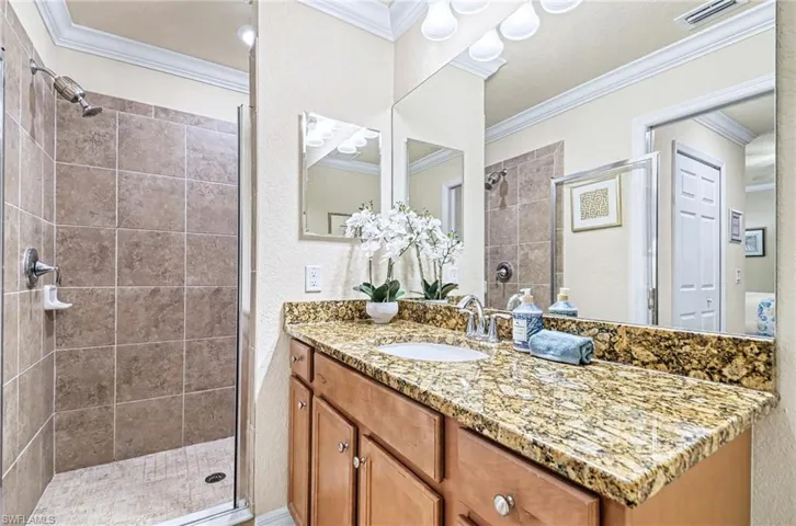 Bathroom featuring a granite countertop vanity with integrated sink, wood-finish cabinetry, and an expansive wall mirror