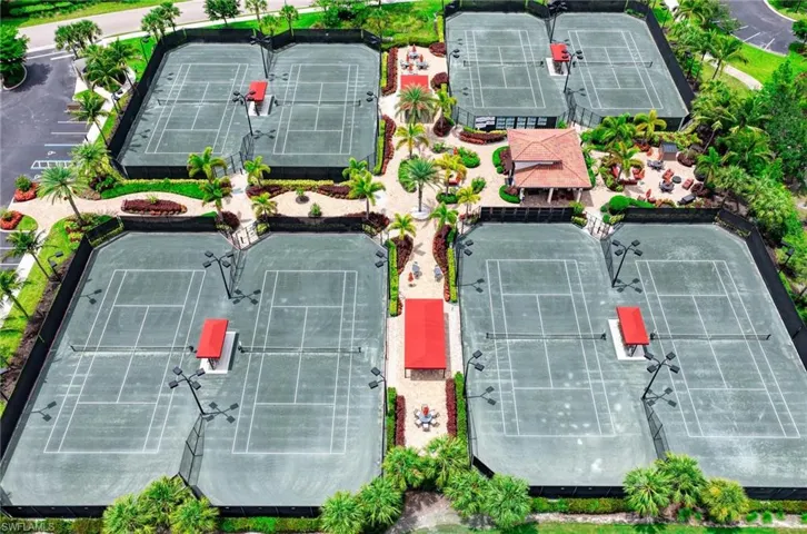 Eight tennis courts with green hard surfaces, dark fencing, and overhead lighting