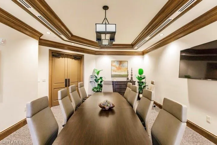 Conference room featuring a large rectangular table, twelve upholstered chairs, and a mounted flat-screen display