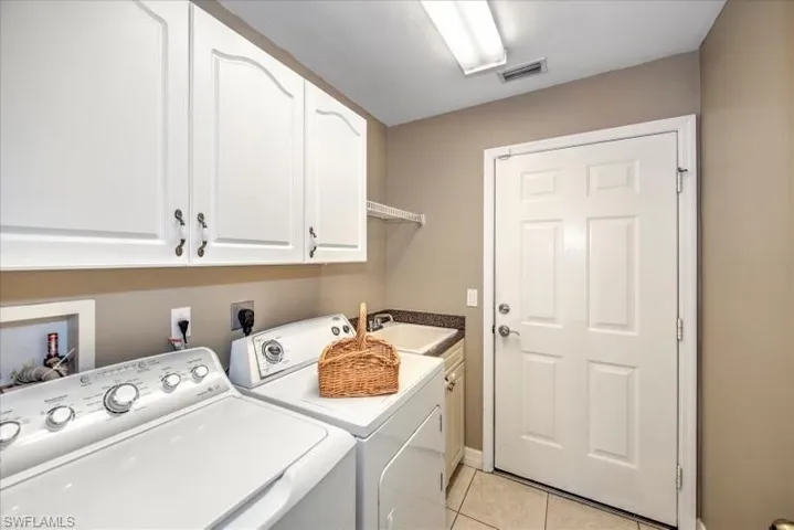 Clothes washing area with cabinets, washer and clothes dryer, washer hookup, sink, and light tile floors
