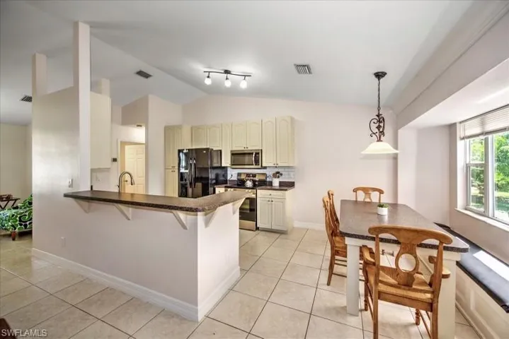 Kitchen featuring cream cabinets, kitchen peninsula, stainless steel appliances, track lighting, and light tile floors