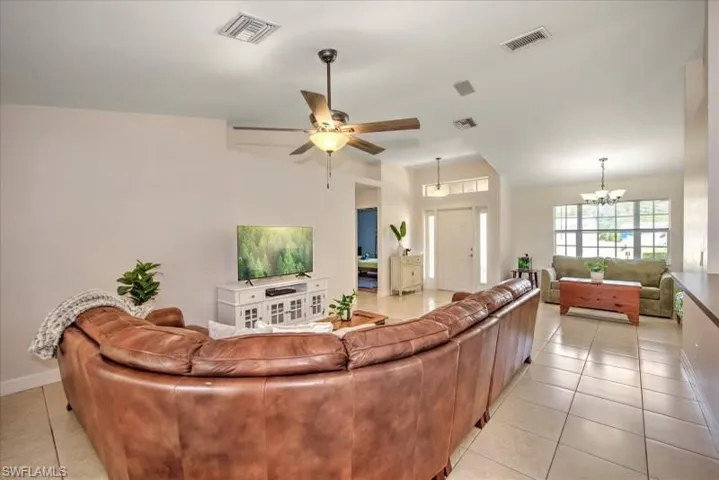 Living room with light tile flooring and ceiling fan with notable chandelier
