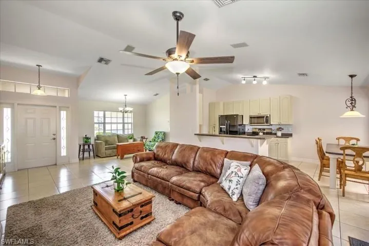 Tiled living room featuring vaulted ceiling, rail lighting, and ceiling fan with notable chandelier
