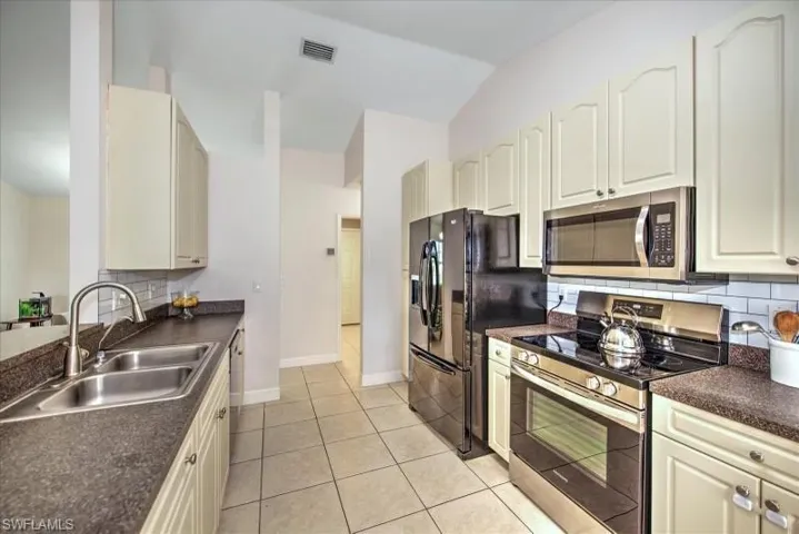 Kitchen featuring stainless steel appliances, white cabinets, backsplash, sink, and light tile floors