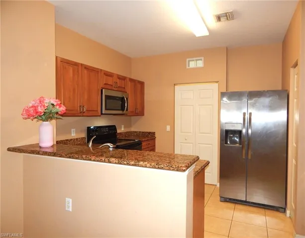 Kitchen with kitchen peninsula, dark stone counters, light tile patterned floors, and appliances with stainless steel finishes